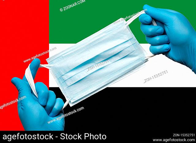 Medic holding respiratory face mask in hands in blue gloves on background national flag of United Arab Emirates UAE. Concept coronavirus quarantine, grippe