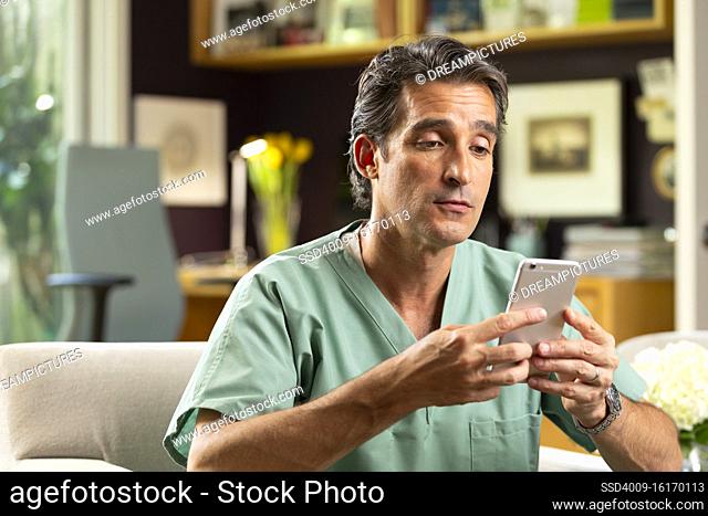 Hispanic Male doctor practicing tele-medicine from his home office, Talking to patient via video call on cell phone