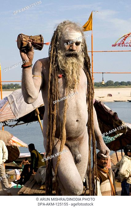 Hindu saint naga baba Shivdasgiri standing on one feet and  holding damroo in hand ; Varanasi on Ganga river ; Uttar Pradesh ; India MR707A