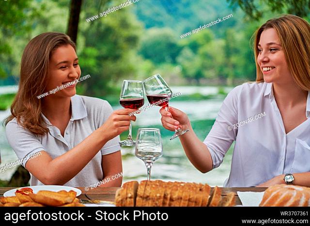 two young happy girlfriends having picnic french dinner party outdoor during summer holiday vacation near the river at beautiful nature