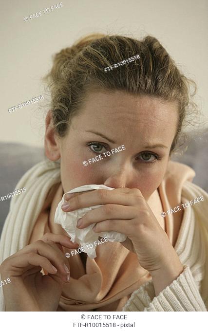 A blonde woman wiping her nose as she suffers from common cold