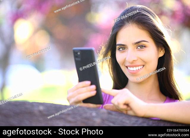 Portrait of a happy mobile phone user looking at camera in a beautiful park