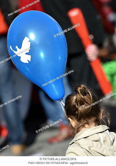 31 March 2018, Germany, Duisburg: A girl holding a balloon with the peace dove during the Rhine-Ruhr Easter March for disarmament
