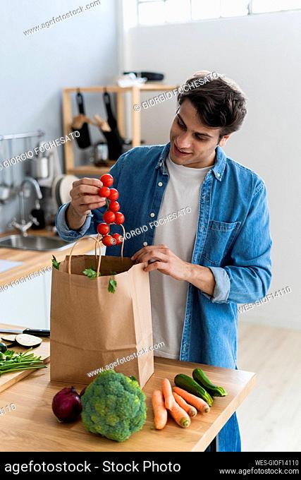 Young man removing cherry tomatoes from bag at kitchen counter
