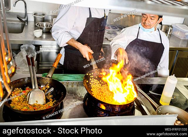 Chef teaching colleague flaming food in wok at kitchen