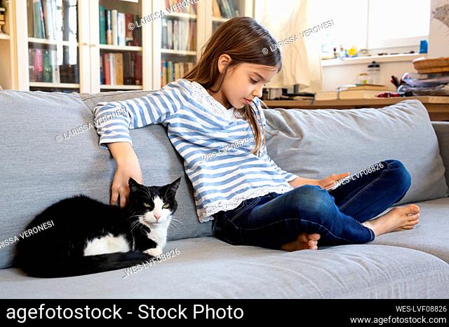 Girl sitting on couch using digital tablet while stroking cat