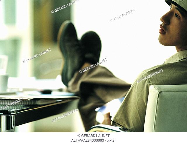 Man sitting in chair with feet on table, looking to the side, rear view