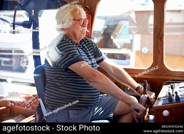 Senior man holding helm sailing motorboat on vacation