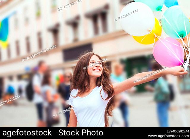Teenage birthday. Pretty girl with big colorful balloons in the street of an old town