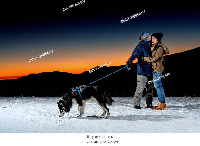 Romantic couple with dog in snow at night