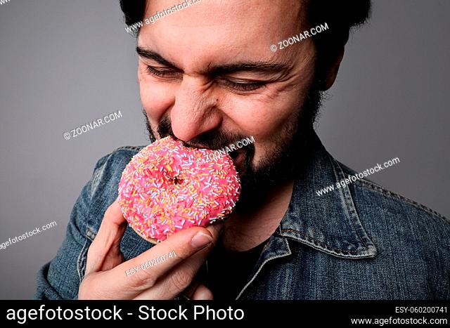Hungry overweight man eating donuts isolated on grey background. High quality photo