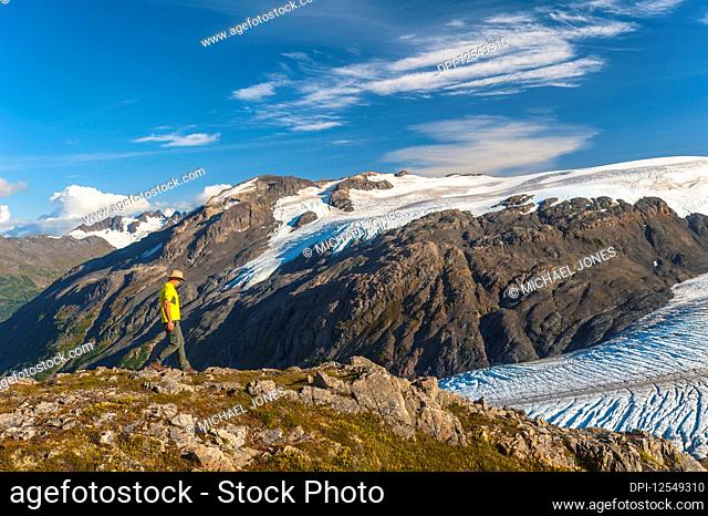 A man hiking near the Harding Icefield Trail with the Kenai Mountains and an unnamed hanging glacier in the background, Kenai Fjords National Park