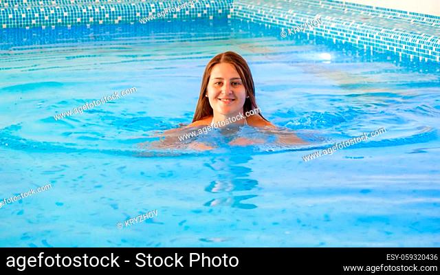 Happy smiling brunette woman with long hair enjoying swimming in indoor swimming pool at hotel resort spa