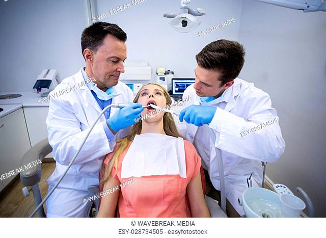 Dentists examining a female patient with tools