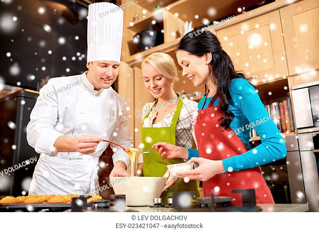 cooking class, culinary, bakery, food and people concept - happy group of women and male chef cook baking muffins in kitchen over snow effect