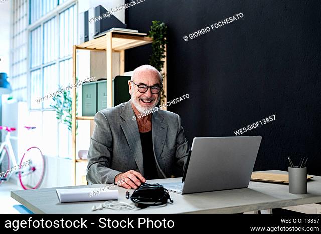 Smiling businessman with laptop sitting at studio