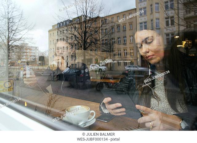 Woman in a cafe behind windowpane using digital tablet