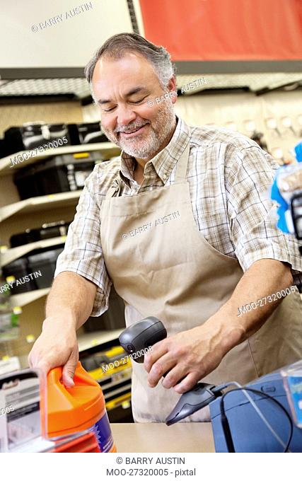 Happy mature store clerk using barcode reader at checkout counter