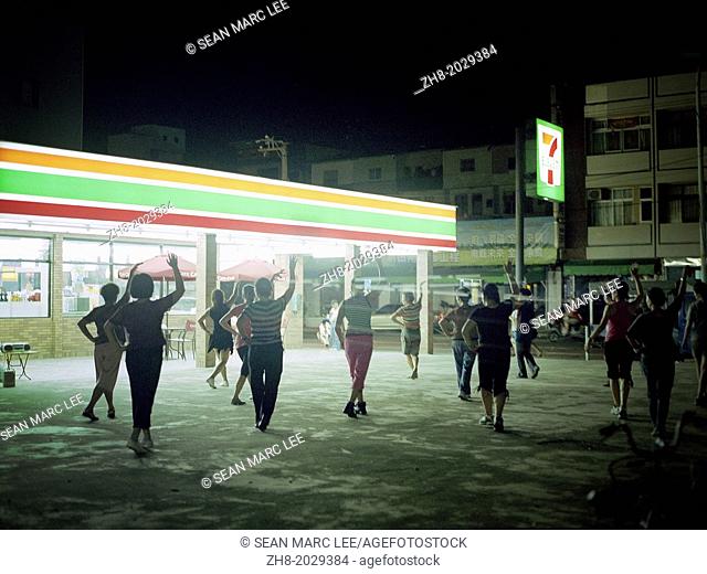 Women work out, dance and practice aerobic exercises in a parking lot in front of a 7-11 chain store in Taiwan