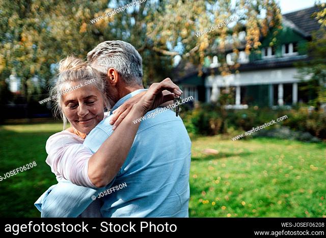 Smiling woman holding house key and hugging man at backyard