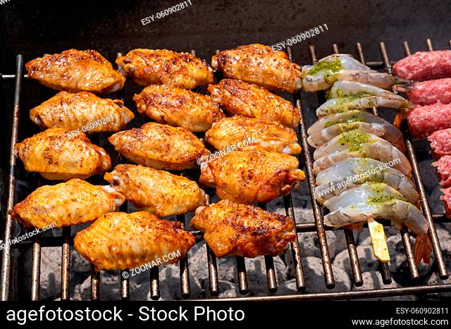 Mixed assortment of marinated meat, chicken, and prawns grilling on hot coals on a BBQ, summer outdoor party, delicious meal preparation