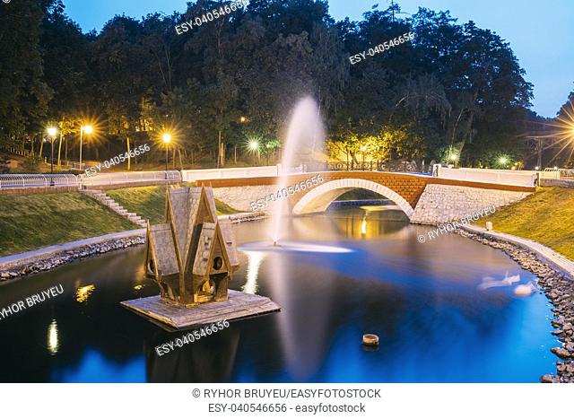 Gomel, Homiel, Belarus. Scenic View Of Park Watercourse Channel Flowing Into River Through Stone Bridge In City Park In Evening Or Night Illumination
