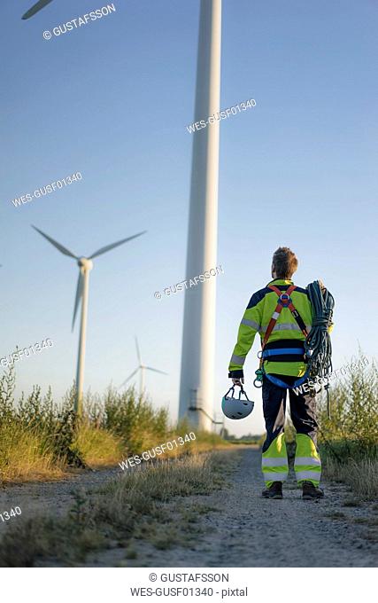 Technician standing on field path at a wind farm with climbing equipment