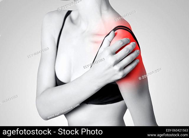 young woman with pain on her arm and shoulder on gray background. Black and white photo with red dot