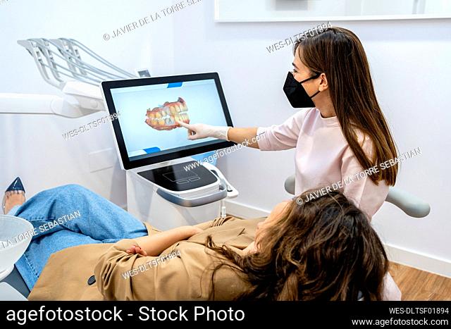 Female dentist explaining on computer screen to patient in clinic during pandemic