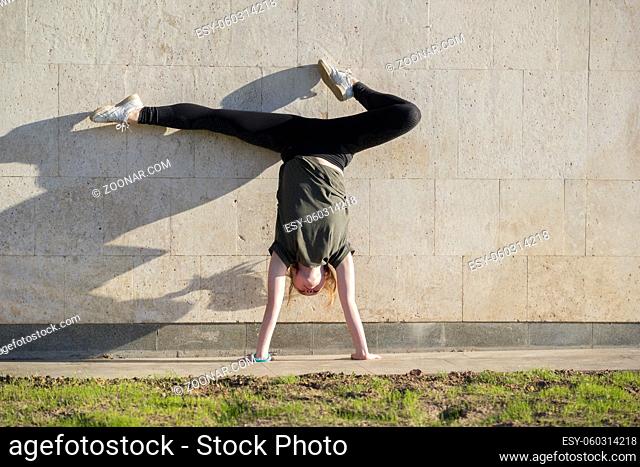 Young female handstand against the wall performs acrobatic elements, close up
