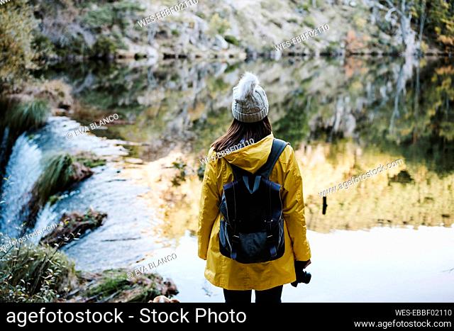 Woman in yellow raincoat facing river and waterfall