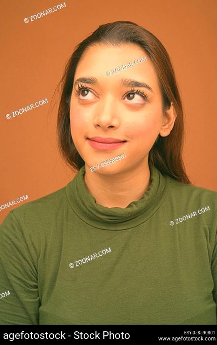 Studio shot of young beautiful Indian woman against brown background