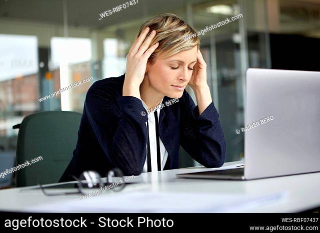 Businesswoman in office with head in hands and closed eyes