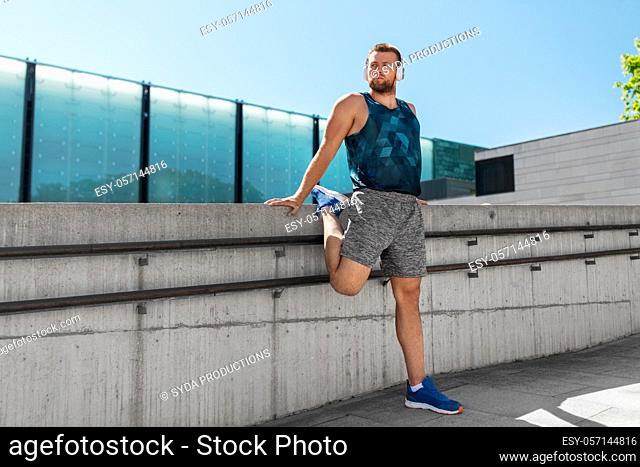 young man in headphones stretching leg outdoors