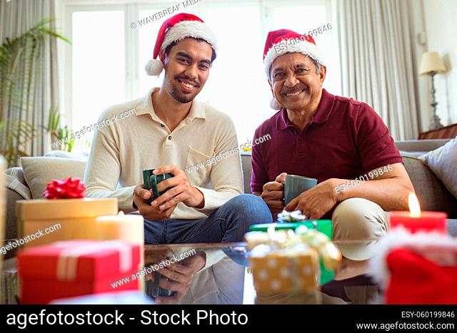 Portrait of happy biracial adult son and senior father in santa hats making christmas video call