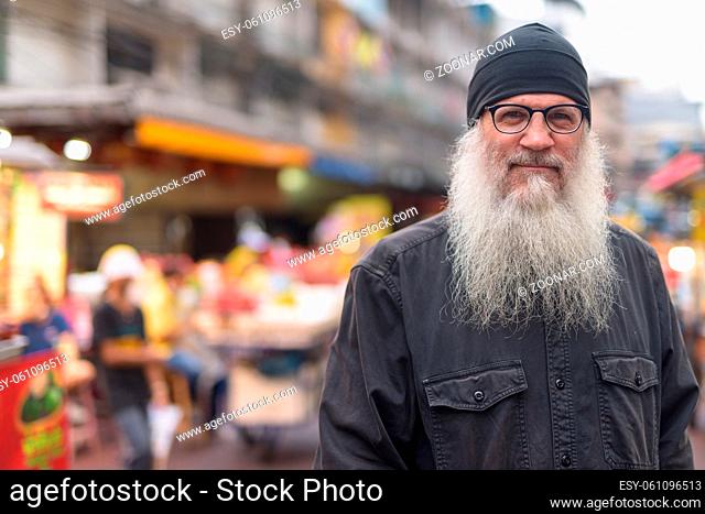 Portrait of mature handsome bearded tourist man exploring Chinatown in Bangkok city