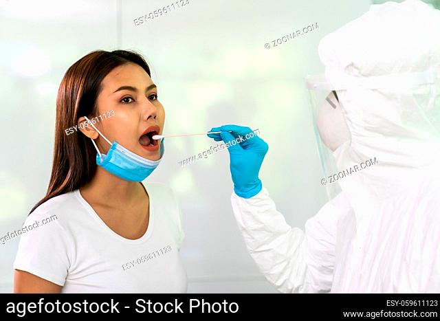 Medical staff with PPE suit test coronavirus covid-19 to asian woman by throat swab at home. New normal health care service at home and medical delivery and...