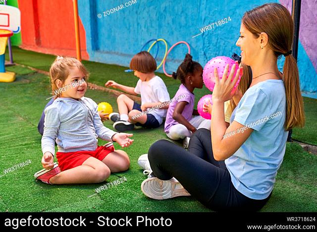 Sportlehrerin spielt mit Kindern Ball im Sportunterricht draußen vor der Kita oder dem Hort