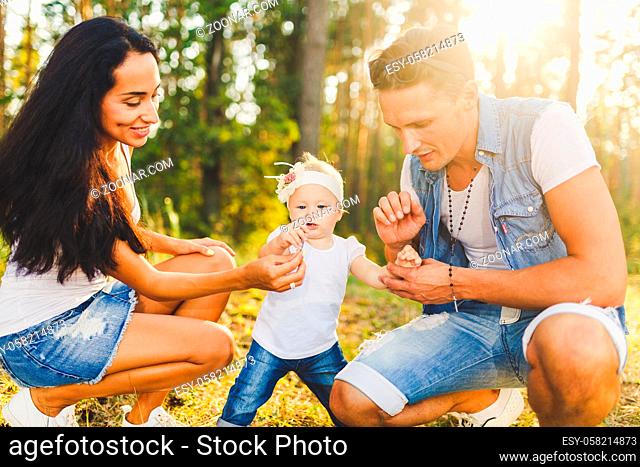 young parents are taught to walk a daughter of one year on nature in a park on a lawn. The first steps of the child's hand with his mother and father