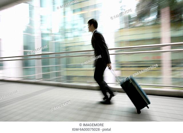 Businessman running with rolling suitcase, blurred motion