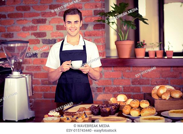 Smiling barista holding cup of coffee