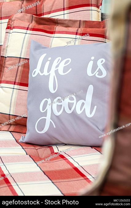 Close-up of a pillow on a outdoor patio bench with the word's Life is Good. modern retro