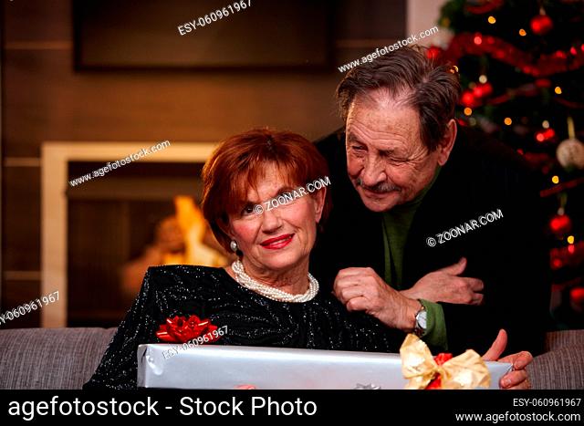Portrait of happy senior couple at christmas at home. Woman holding christmas present, smiling