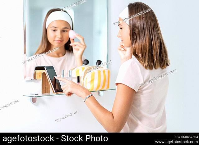 teenage girl with smartphone using make up sponge
