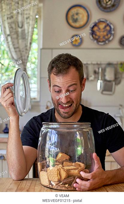 Man sitting in kitchen, looking in cookie jar, laughing