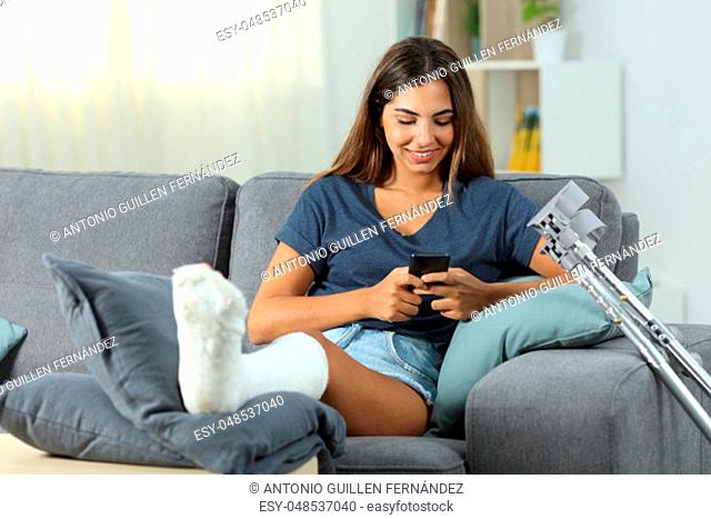 Disabled woman using a smart phone sitting on a couch in the living room at home