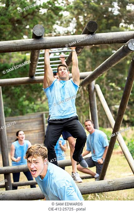 Determined man crossing monkey bars on boot camp obstacle course