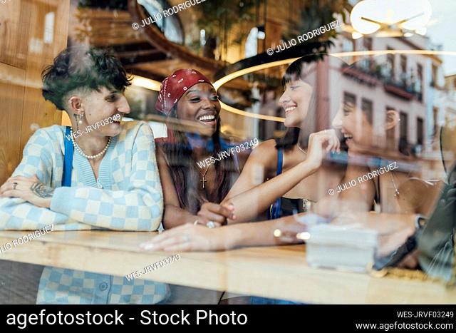 Happy friends talking in cafe seen through glass