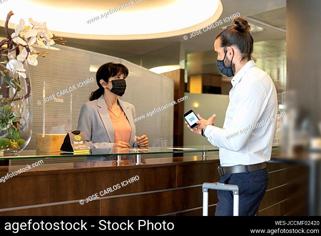 Male customer showing QR code to female receptionist in hotel during pandemic