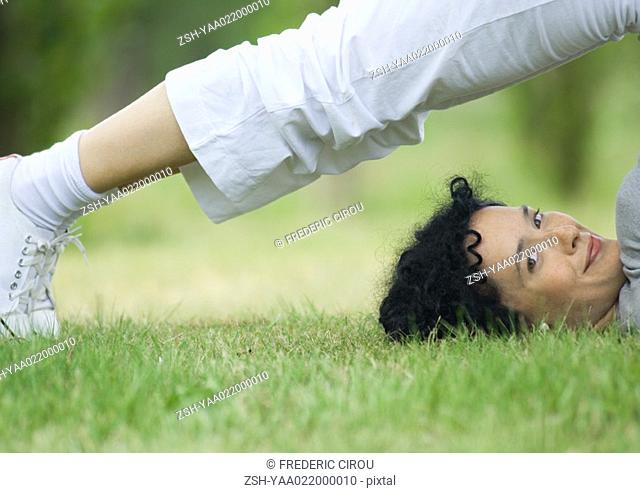 Young woman doing plow pose outdoors, smiling at camera